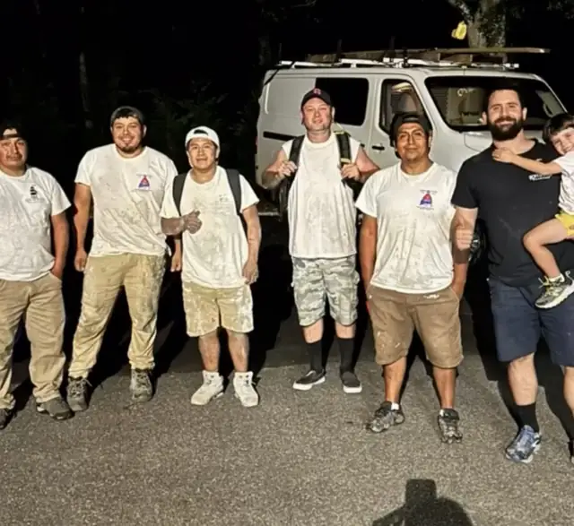 Equipe suja de tinta à noite, ao lado da van, Vini com o filho no colo